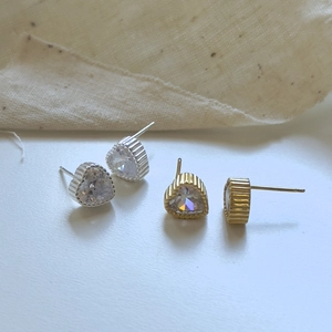 Detail of silver and gold heart-shaped zircon stud earrings with vertical texture edges