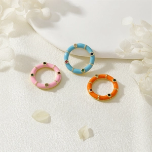 Detailed view of colorful enamel rings with inlaid zircons on white silk background