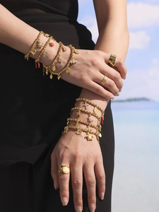 Nahaufnahme goldener Mehrschichtarmbänder mit Zirkonia-Meeresanhängern am Strandhintergrund