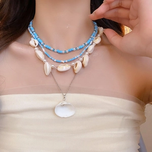 Detail of bohemian layered necklace set featuring blue beads and shell charms on a model