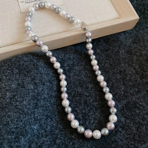 Close-up of pearl necklace in white, grey, and purple tones with a metallic clasp