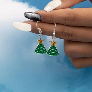 Elegant green enamel Christmas tree drop earrings with gold stars against a bright blue sky