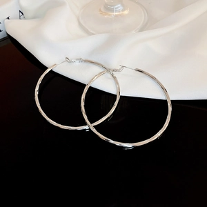 Macro shot of large silver twisted hoop earrings on black reflective surface with silk