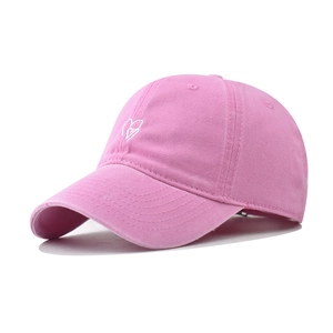 Detail view of pink washed cotton baseball cap with white heart embroidery on the side