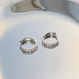 Macro shot of silver hoop earrings with pave white zircon on a reflective mirror surface