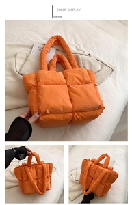 Detailed close-up of quilted orange puffer tote bag with thick padded handles on a bed
