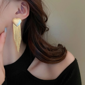 Macro shot of gold tassel drop earrings with heart stud on a model's ear