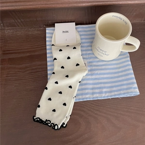 Detail of cream knit crew socks with black heart patterns and ruffled edges on wood