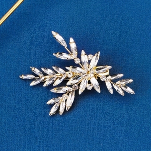 Detail of gold floral hair clip featuring crystal leaves on blue fabric background