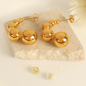Fashionable golden pea-shaped bead earrings on a natural stone surface