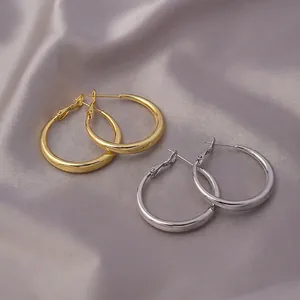 Minimalist large hoop earrings in polished gold and silver finish on silk background