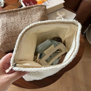 Detail view of the beige wool tweed pouch interior filled with small personal items
