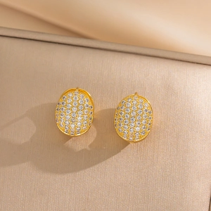 Elegant gold oval hoop earrings with shimmering white zircon stones on beige background