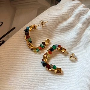 Detail of gold C-shaped earrings with colorful stone beads on textured fabric