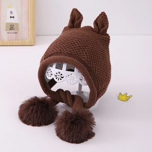 Detailed view of dark brown knitted baby earflap hat with cute ears and fuzzy pom-poms