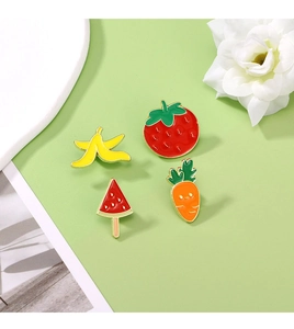 Detail of four enamel fruit and vegetable pins featuring banana, strawberry, and carrot