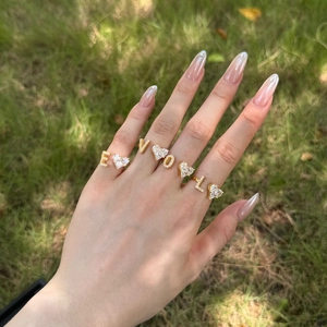 Golden S925 sterling silver rings with zircons spelling EVOL on fingers in sunlight