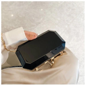 Detail of model holding a black octagonal acrylic clutch with gold frame and spherical clasp