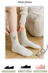 Close-up of thick white fuzzy socks with black heart embroidery on light wooden floor