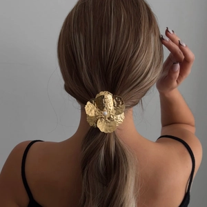 Elegant gold metal flower hair tie with pearl center worn on a ponytail hair