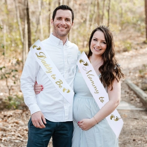 Outdoor close-up of white and gold Mommy to Be sash set with Daddy to Be ribbon