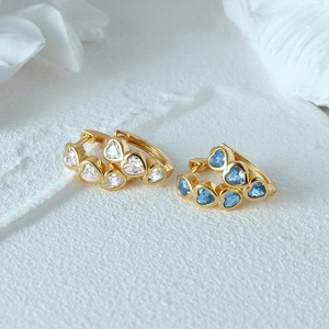 Detail of gold huggie earrings featuring blue and clear heart-shaped gemstones