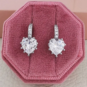Macro detail of heart-shaped silver earrings with clear crystals in pink velvet box