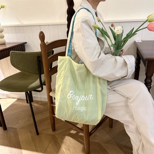 Light green canvas tote bag with Bonjour print shown on shoulder in a cafe setting