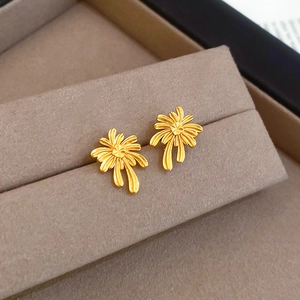 Macro shot of gold plated palm tree stud earrings on a beige velvet jewelry box tray