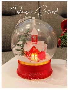 Close-up of lighted Christmas snow globe with a red house and snowy tree inside
