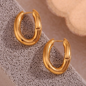 Close-up of golden oval earrings with a polished finish on a textured grey background