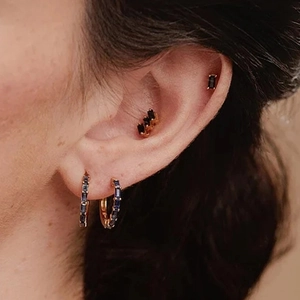 Close-up of gold earrings set with blue rectangular zircon on model ear