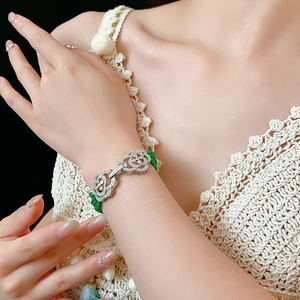 Detail of a floral clasp bracelet with green beads worn on a wrist with a lace sleeve