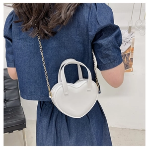 Close-up of white heart-shaped jelly bag with gold chain worn by a model in denim