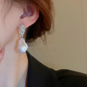 Macro detail of silver geometric earring with a large baroque pearl on a model