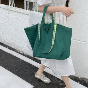 Detail of green canvas tote bag featuring green and white checkered straps and merciparis logo