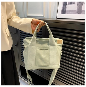 Close-up of small light green canvas tote bag held by model with leather tag detail