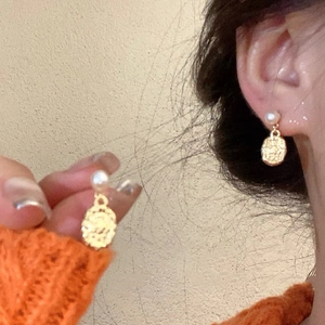 Detailed close-up of retro gold earrings with white pearl and oval relief pendant on ear