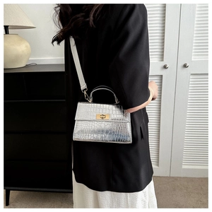 Detailed view of silver crocodile embossed leather bag with gold buckle and top handle