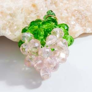 Detail of a handmade grape crystal pendant with green leaves and pink beads on a stone