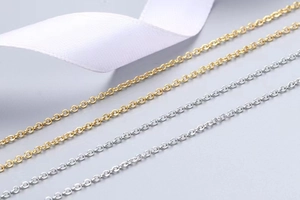Detailed close-up of delicate gold and silver cable chain necklaces on a soft grey background