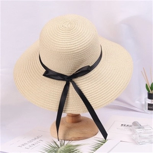 Elegant wide brim straw hat with black ribbon bow on a stylish wooden stand