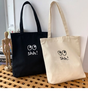 Primer plano de bolsos tote de lona negros y beige con diseño de ojos en banco de madera