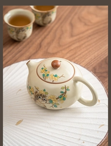 Artistic detail of a Ru kiln ceramic teapot with cat and floral motifs on a white fan