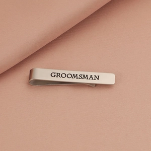 Detailed view of silver tie clip with black GROOMSMAN engraving on pink fabric