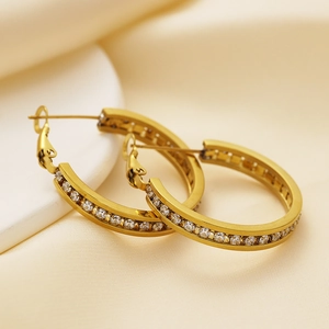 Detailed macro view of golden stainless steel hoop earrings with white zircon crystals