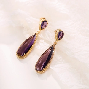 Detail of elegant gold drop earrings with large purple pear-cut stones and crystal halo