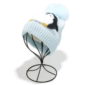 Detail of light blue knit hat featuring a cute cartoon penguin pattern and large pom pom
