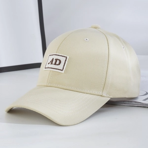 Detail of beige baseball cap featuring AD letter patch and curved brim design