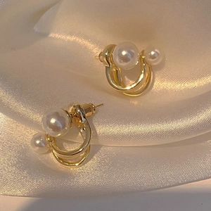 Close-up of geometric golden earrings with dual white pearls on beige silk fabric